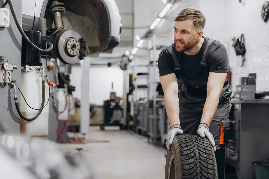 A mechanic wheeling a tyre across a busy workshop