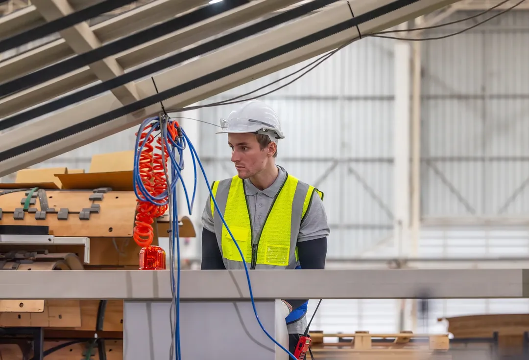 A worker in a hard hat and hi-vis on the shop floor of a fabrication workshop